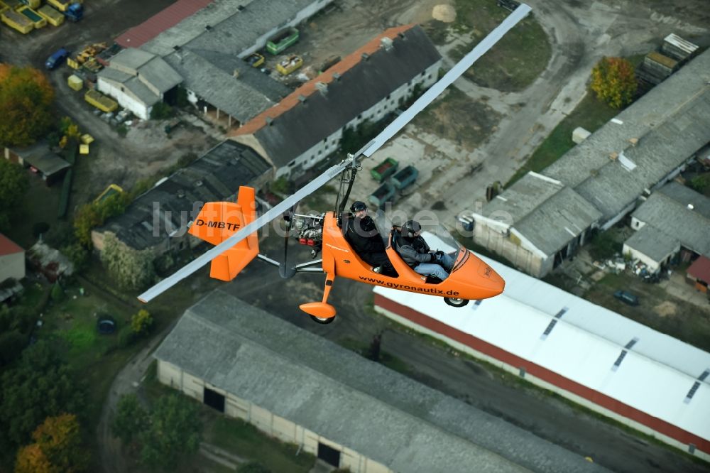 Saarmund aus der Vogelperspektive: Orange farbiger Ultraleicht - Gyrokopter der Flugschule Gyronautix mit der Kennung D-MBTF im Fluge über dem Luftraum in Saarmund im Bundesland Brandenburg