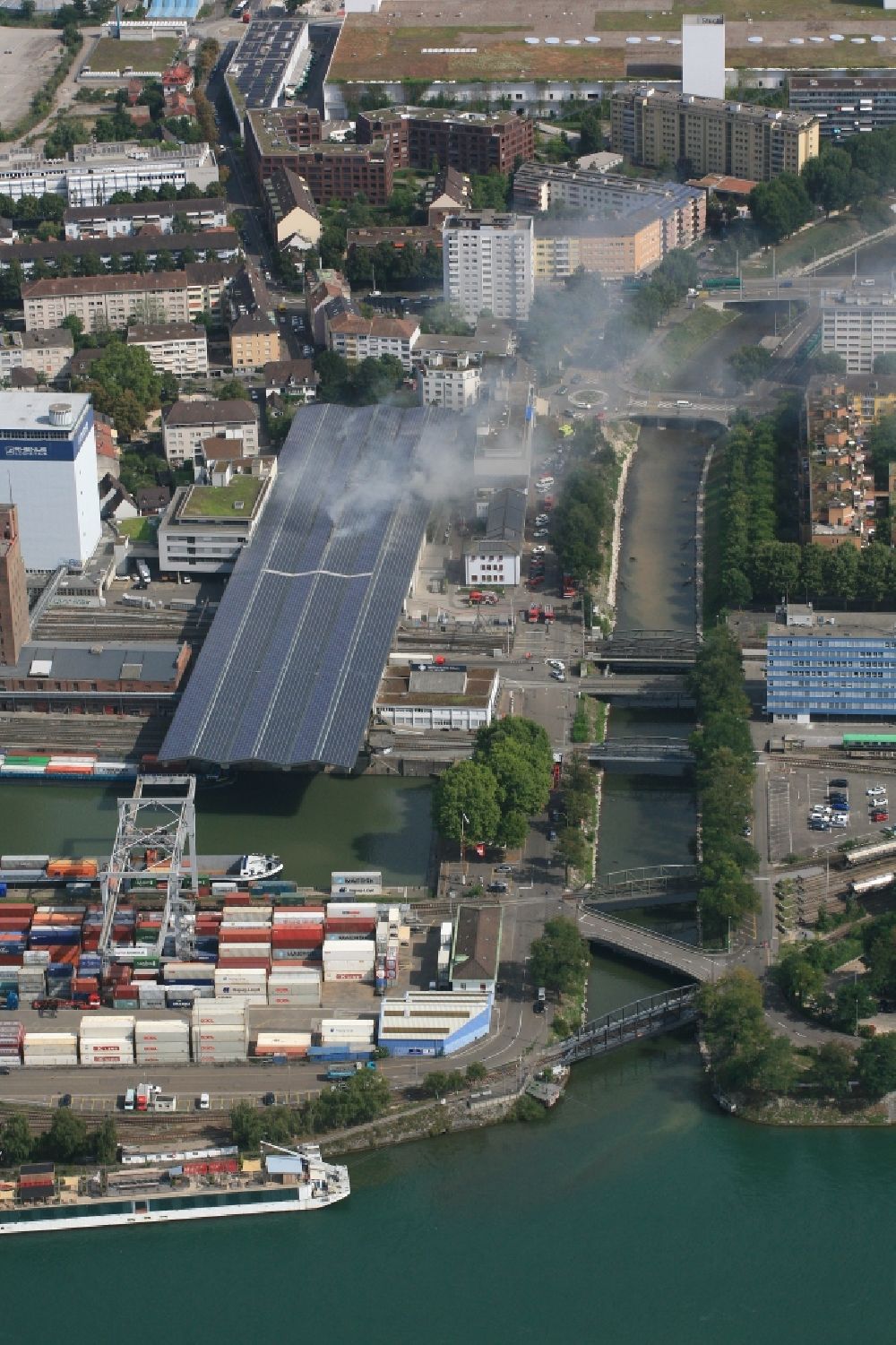 Luftaufnahme Basel - Rauch- und Flammenbildung während der Löscharbeiten zum Brand in der Lagerhalle von Rhenus in Basel, Schweiz