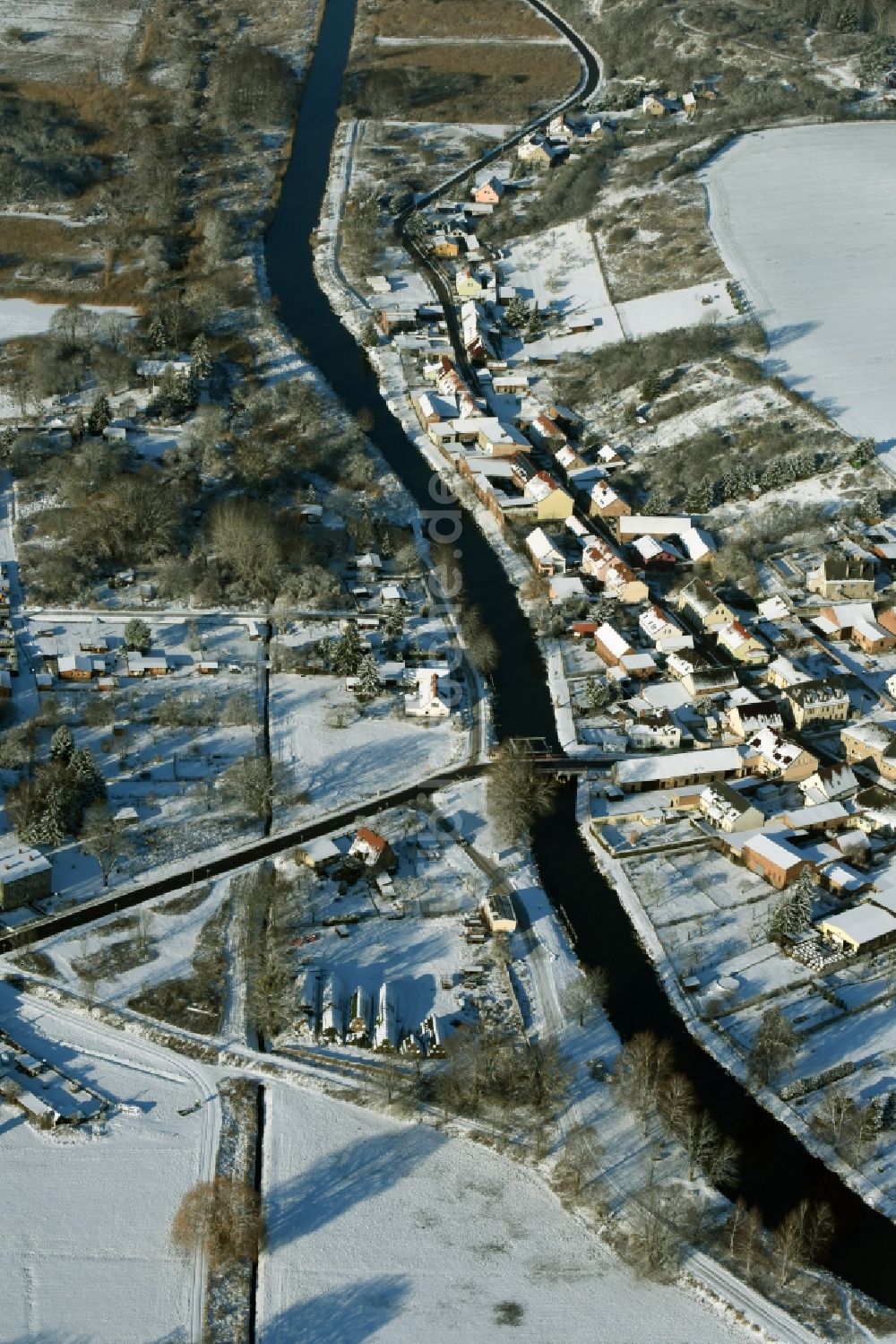 Niederfinow von oben - Verlauf des Flusses Alte Finow entlang des Ortsrandes des winterlich verschneiten Dorfes Niederfinow im Bundesland Brandenburg